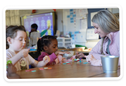 Two young students with adult putting together puzzle pieces