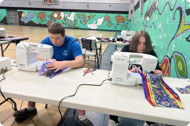 Two students sewing their ribbon shirts/skirts
