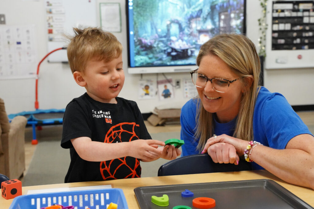 Educator and young child participating in a hands-on learning activity at a classroom table.